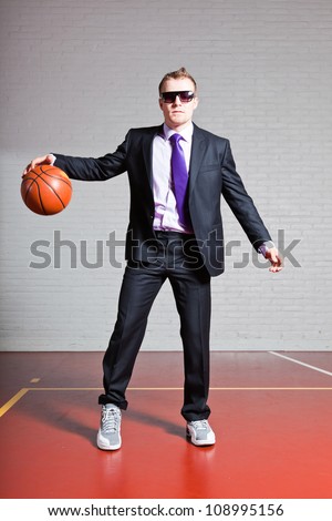 Business man with basketball. Wearing dark sunglasses. Good looking young man with short blond hair. Gym indoor.