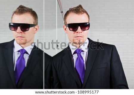 Cool good looking business man with dark sunglasses standing against mirror.