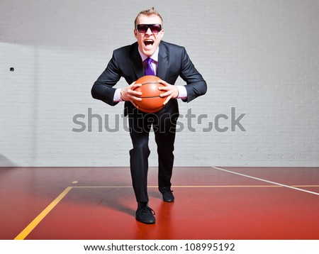 Angry business man with basketball. Wearing dark sunglasses. Good looking young man with short blond hair. Gym indoor.