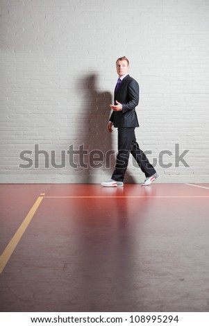 Good looking young man with blond short hair wearing dark suit and basketball shoes. Gym indoor.