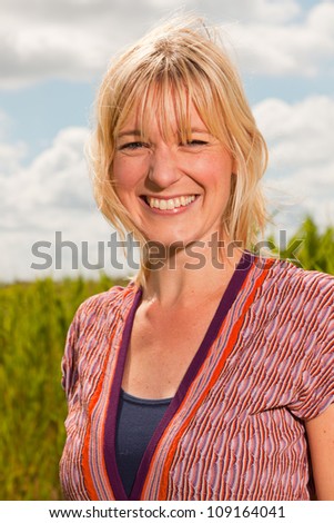 Happy pretty young blond woman enjoying nature. Field with high grass. Blue cloudy sky. Dressed in red.