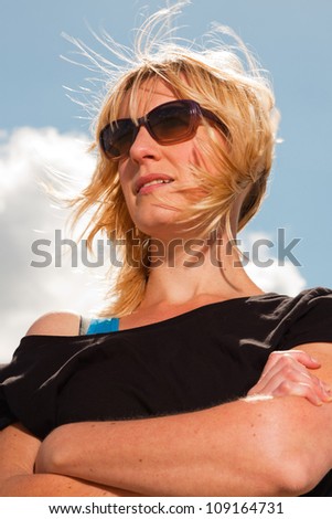 Happy pretty blond woman on the beach. Enjoying nature. Blue cloudy sky. Wearing black sweater and sunglasses.