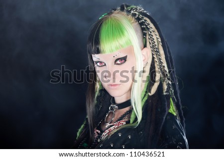Cyber punk girl with green blond hair and red eyes isolated on black background with smoke. Expressive face. Studio shot.
