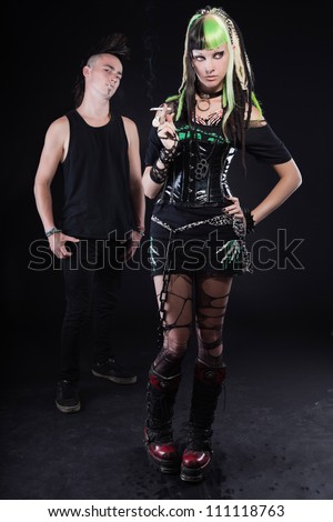 Couple of cyber punk girl with green blond hair and punk man with mohawk haircut. Expressive faces. Smoking cigarette. Isolated on black background. Studio shot.