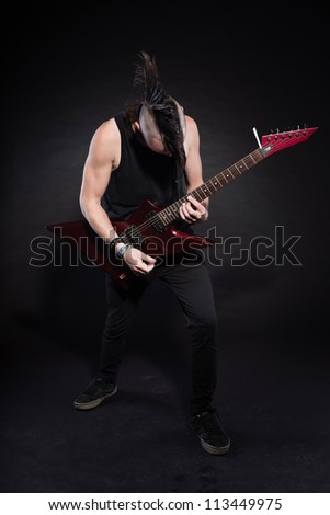 Punk rock man with red electric guitar and mohawk haircut. Expressive face. Isolated on black background. Studio shot.