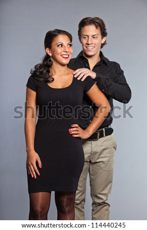 Pretty young couple dressed in black. Brother and sister. Good looking. Brown hair and eyes. Studio portrait isolated on grey background.