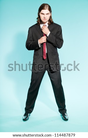 Cool business man with long brown hair confident looking. Wearing black striped suit and dark red tie. Standing out guy. Isolated on light blue background. Studio shot.