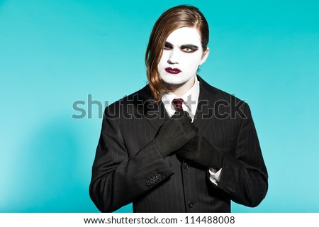 Gothic vampire looking business man wearing black striped suit and dark red tie. Another kind. Scary white face. Isolated on light blue background. Studio shot.