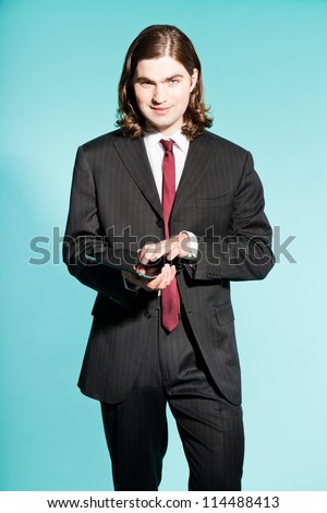 Smiling business man with long brown hair holding tablet. Wearing black striped suit and dark red tie. Standing out guy. Isolated on light blue background. Studio shot.