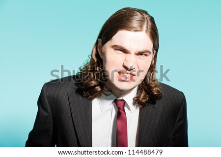 Angry frustrated business man with long brown hair. Wearing black striped suit and dark red tie. Standing out guy. Isolated on light blue background. Studio shot.