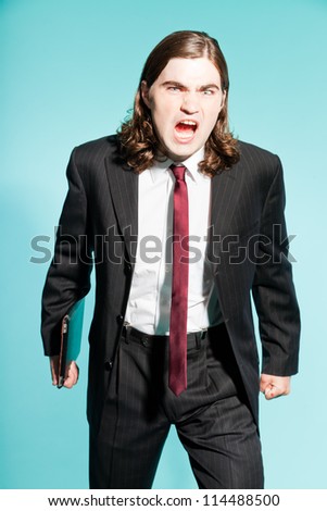Angry frustrated business man with long brown hair holding tablet. Wearing black striped suit and dark red tie. Standing out guy. Isolated on light blue background. Studio shot.