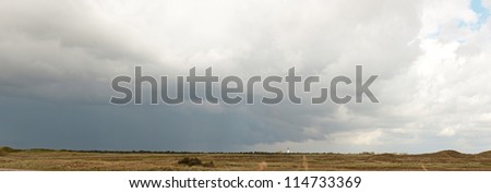 Panoramic shot of dutch dune landscape with stormy blue cloudy sky. White old church on the horizon. Texel. Wadden island. The Netherlands.