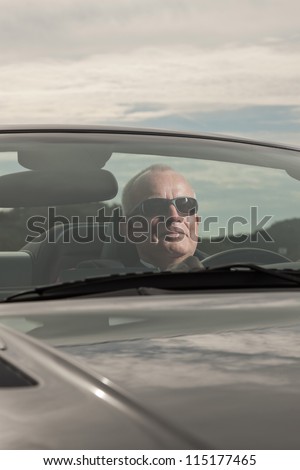 Senior good looking happy relaxed retired man with his sports car in dune landscape with cloudy sky. Wearing smoking suit and glasses. Classy different man.