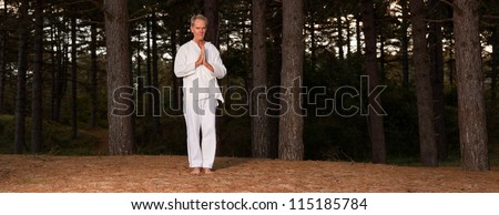 Panoramic shot of meditating senior man in forest. Dressed in white. Peace of mind. Finding balance. Inner rest. Healthy retired living.