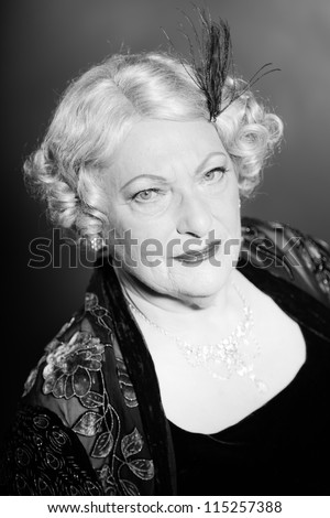 Good looking senior woman glamour vintage style. Black and white studio shot. Short blonde curly hair. Chic look. Dressed in black.