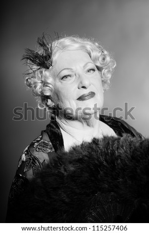 Good looking senior woman glamour vintage style. Holding a black fan. Black and white studio shot. Short blonde curly hair. Chic look. Dressed in black.