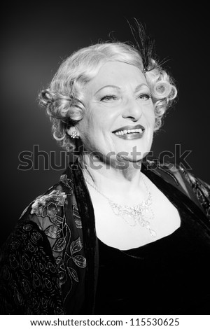 Good looking senior woman glamour vintage style. Black and white studio shot. Short blonde curly hair. Chic look. Dressed in black.