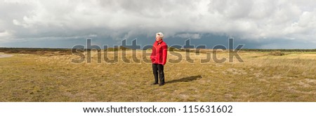 Panoramic shot of senior retired woman enjoying the outdoors. Dutch dune landscape with stormy cloudy sky. Lonely woman. The Netherlands. Wadden island. Texel.