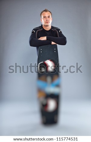 Serious confident man with short hair wearing wetsuit. Holding kiteboard. Kite surfer. Studio shot. Isolated on grey background.