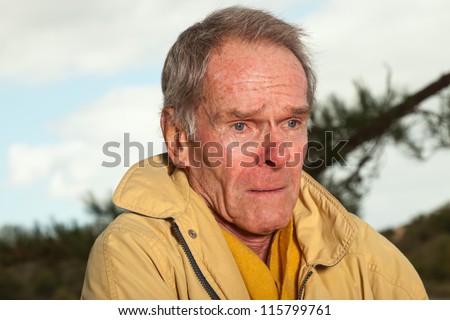 Senior man with yellow coat. Having cold. Sad looking. Warming up. Short grey hair. Autumn. Outdoors. Dune landscape. Cloudy sky. Healthy living.