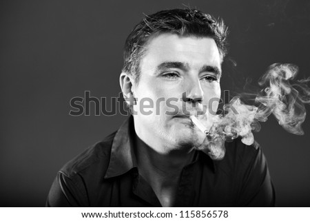 Smoking handsome man with short brown hair wearing black shirt. Good looking. Fashion studio portrait. Isolated on grey background. Glamour black and white portrait.