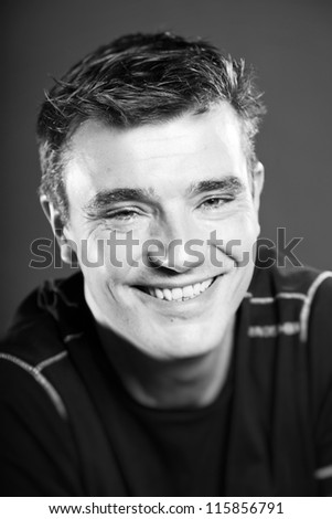 Smiling handsome man with short brown hair wearing black shirt. Good looking. Fashion studio portrait. Isolated on grey background. Glamour black and white portrait.