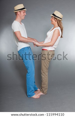 Happy young couple. Casual dressed. Wearing summer hat. White shirt. Blue pants. Brown pants. Man short blonde hair. Woman long brown hair. Studio shot isolated on grey background.