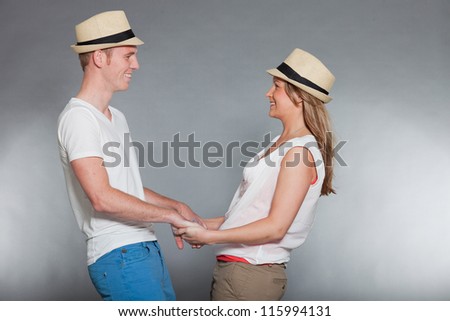 Happy young couple. Casual dressed. Wearing summer hat. White shirt. Blue pants. Brown pants. Man short blonde hair. Woman long brown hair. Studio shot isolated on grey background.
