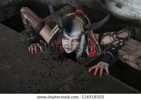 Scary hungry female demon crawling out of the floor. Bloody wall.