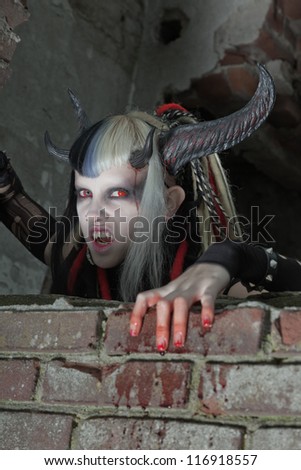 Scary hungry female demon crawling over old dirty brick wall.