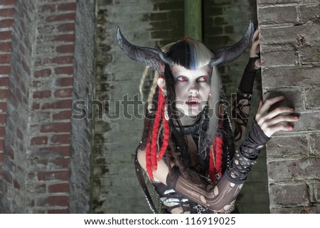 Scary female demon in front of old dirty brick wall.