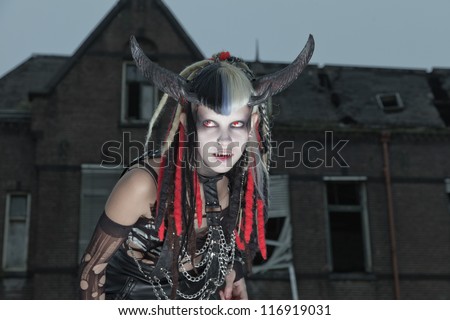 Scary hungry female demon in front of spooky house.