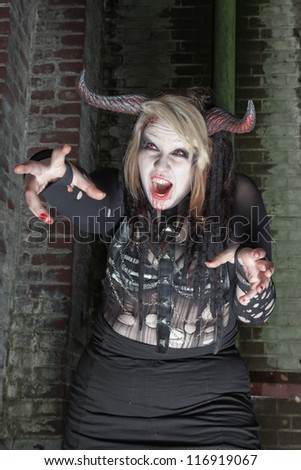 Scary female demon in front of old dirty brick wall.