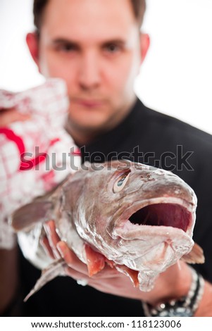 Young male cook with black jacket holding a big fish isolated on white.