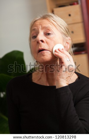 Good looking senior woman doing make-up in front of mirror.