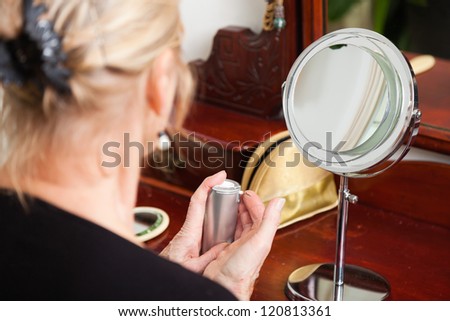 Good looking senior woman doing make-up in front of mirror.