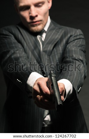 Man in suit shooting with gun. Studio shot against black.