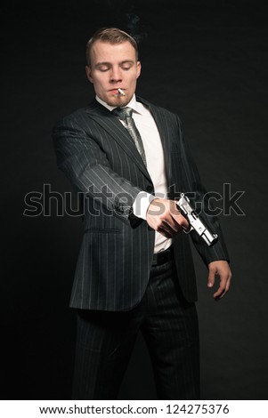 Man in suit shooting with gun. Smoking cigarette. Studio shot.