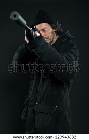 Sniper with beard in black holding gun. Studio shot.