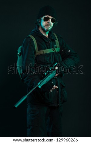 Sniper with beard in black holding gun. Studio shot.