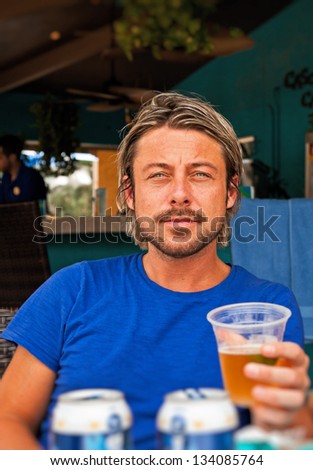 Summer man with blonde hair drinking a beer. Blue shirt.