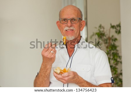 Senior man eating fresh fruit dish. Sitting in living room.