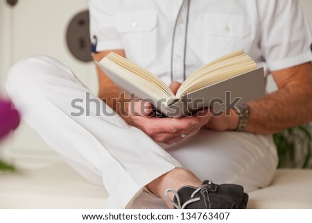 Hands of senior man reading book in living room.