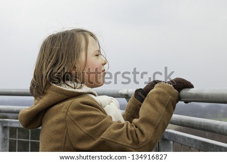 Playful funny young boy with long hair viewing landscape from tower.