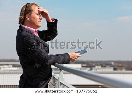 Business man with blue suit outdoor on rooftop using tablet.