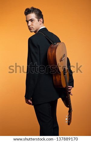 Retro country musician with guitar on is back wearing black suit. Studio shot.