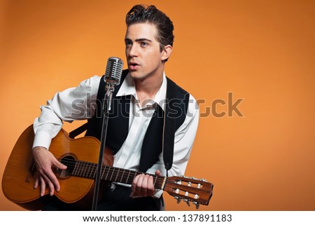 Retro country singer with guitar wearing black suit. Studio shot.