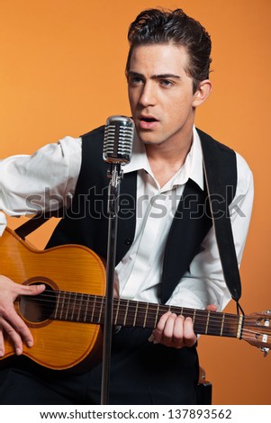 Retro country singer with guitar wearing black suit. Studio shot.