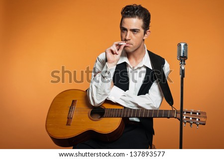 Retro country singer with guitar wearing black suit. Smoking cigarette. Studio shot.