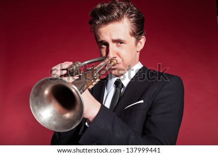 Retro fifties trumpet player wearing black suit. Playing trumpet. Red wall.